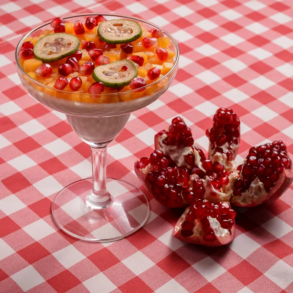 Sweet dessert pannacotta with pomegranate jelly and served with pomegranate syrup and seeds in a tall glass over red plaid tablecloth. Italian concept. Fruit dessert.