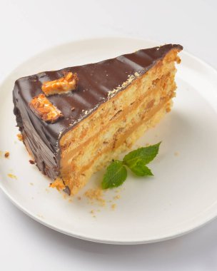 Beyaz arka planda beyaz bir tabakta servis edilen naneli ve çikolatalı pasta. Çay ya da kahve saati için bir parça çikolatalı kek. Tatlı nefis..