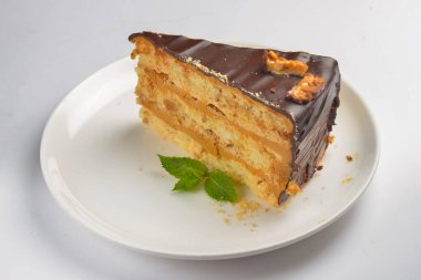 Beyaz arka planda beyaz bir tabakta servis edilen naneli ve çikolatalı pasta. Çay ya da kahve saati için bir parça çikolatalı kek. Tatlı nefis..