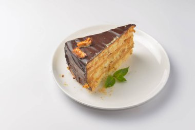 Beyaz arka planda beyaz bir tabakta servis edilen naneli ve çikolatalı pasta. Çay ya da kahve saati için bir parça çikolatalı kek. Tatlı nefis..