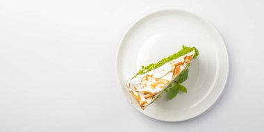 Bir parça yeşil çay keki. Beyaz arka planda beyaz tabağın etrafında servis edilen krema kremalı ve nane yaprağıyla bir parça kibrit çayı keki. Çay ya da kahve için lezzetli bir tatlı..