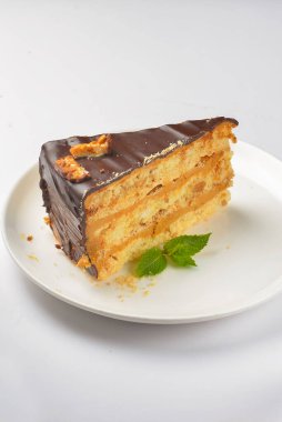 Beyaz arka planda beyaz bir tabakta servis edilen naneli ve çikolatalı pasta. Çay ya da kahve saati için bir parça çikolatalı kek. Tatlı nefis..