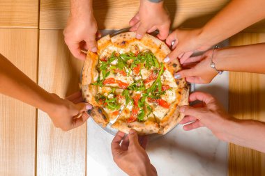 Arkadaş ellerinin pizza dilimlerini alırken görüntüsü. Üst manzara, düz yatış. İtalyan mutfağı konsepti, restoranda lezzetli pizza yemek. Konsepti tüketiyorum.