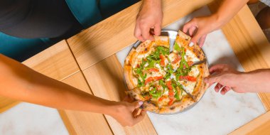 Arkadaş ellerinin pizza dilimlerini alırken görüntüsü. Üst manzara, düz yatış. İtalyan mutfağı konsepti, restoranda lezzetli pizza yemek. Konsepti tüketiyorum.