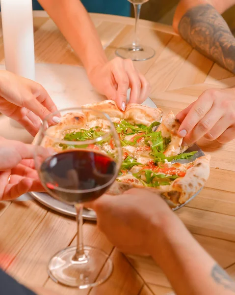 Friends hands with glasses of wine and pizza, close up.l Still life, group of people in a restaurant eating pizza and drinking wine. Traditional Italian cuisine concept, leisure time.