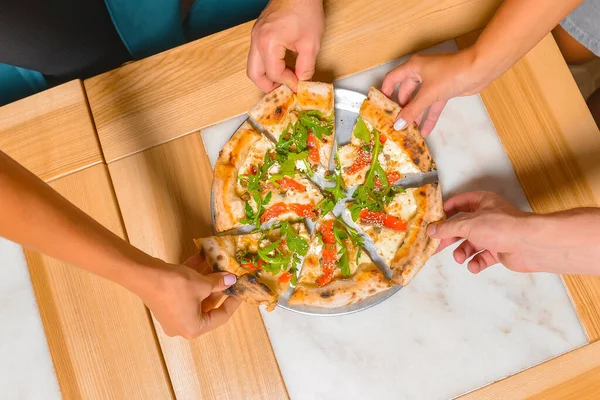 Arkadaş ellerinin pizza dilimlerini alırken görüntüsü. Üst manzara, düz yatış. İtalyan mutfağı konsepti, restoranda lezzetli pizza yemek. Konsepti tüketiyorum.