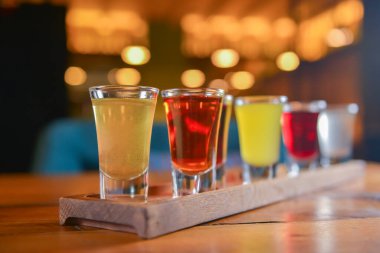 Küçük kadehlerle tentür alkoliği. Doğal meyve alkollü içecekler, bulanık arka planda ahşap bir masada servis edilen içkiler. Ahududu, çilek ve diğer meyveler, organik alkol özü..