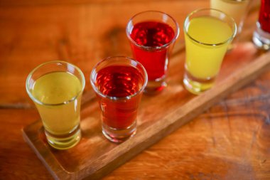 Küçük kadehlerle tentür alkoliği. Doğal meyve alkollü içecekler, bulanık arka planda ahşap bir masada servis edilen içkiler. Ahududu, çilek ve diğer meyveler, organik alkol özü..