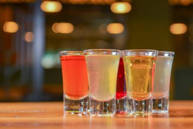 Küçük kadehlerle tentür alkoliği. Doğal meyve alkollü içecekler, bulanık arka planda ahşap bir masada servis edilen içkiler. Ahududu, çilek ve diğer meyveler, organik alkol özü..