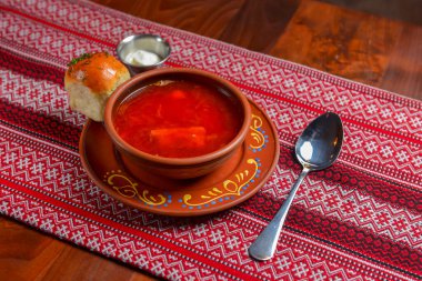 Ukrayna pancar çorbası - geleneksel kırmızı masa örtüsü arka planında seramik bir kasede servis edilen ekşi kremalı borş çorbası. Geleneksel Ukrayna mutfağı konsepti, lezzetli akşam yemeği..