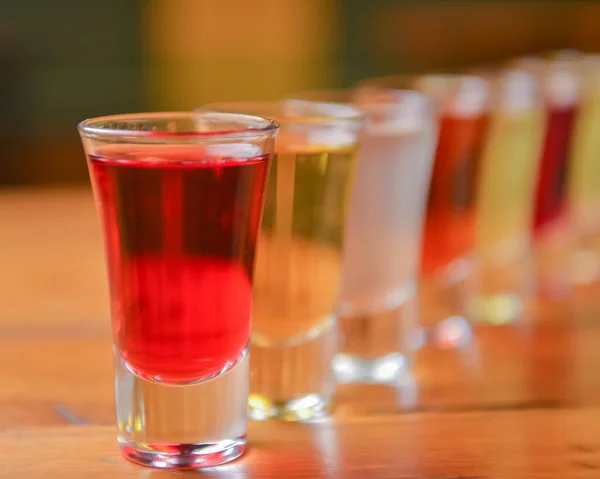 Tincture alcoholic in small shot glasses. Natural fruit alcohol drinks, shots served on a wooden table over blurred background. Raspberry, strawberry and other berry tincture, organic alcohol extract.
