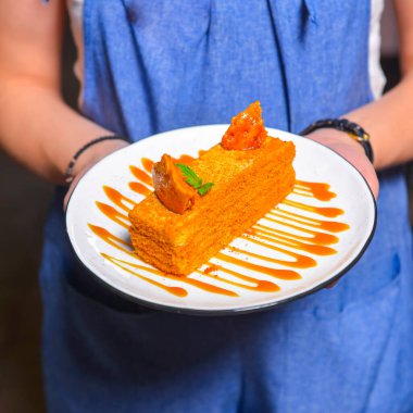 Tabakta ballı kek. Restorandaki ya da kafedeki garson elinde bir parça ballı kek tutuyor. Çay ya da kahve için lezzetli bir tatlı. Restoran servisi..