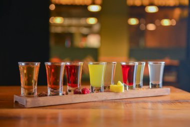 Küçük kadehlerle tentür alkoliği. Doğal meyve alkollü içecekler, bulanık arka planda ahşap bir masada servis edilen içkiler. Ahududu, çilek ve diğer meyveler, organik alkol özü..