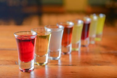 Küçük kadehlerle tentür alkoliği. Doğal meyve alkollü içecekler, bulanık arka planda ahşap bir masada servis edilen içkiler. Ahududu, çilek ve diğer meyveler, organik alkol özü..