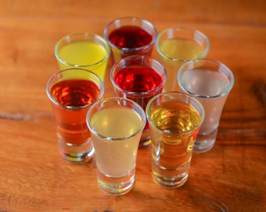 Küçük kadehlerle tentür alkoliği. Doğal meyve alkollü içecekler, bulanık arka planda ahşap bir masada servis edilen içkiler. Ahududu, çilek ve diğer meyveler, organik alkol özü..