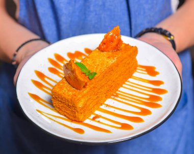 Tabakta ballı kek. Restorandaki ya da kafedeki garson elinde bir parça ballı kek tutuyor. Çay ya da kahve için lezzetli bir tatlı. Restoran servisi..