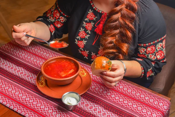 Durgun hayat. Ukrayna pancar çorbası içiyorum. Ekşi kremalı borş. Geleneksel kırmızı masa örtüsü arka planında servis ediliyor. Geleneksel Ukrayna mutfağı kavramı. Etnik giyimli kadın.