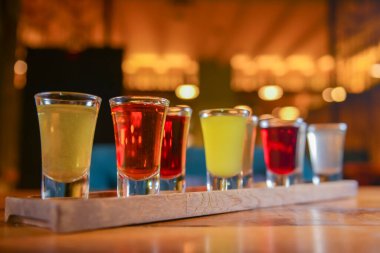 Küçük kadehlerle tentür alkoliği. Doğal meyve alkollü içecekler, bulanık arka planda ahşap bir masada servis edilen içkiler. Ahududu, çilek ve diğer meyveler, organik alkol özü..