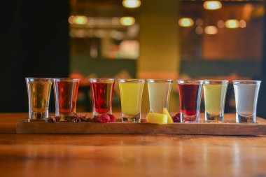 Küçük kadehlerle tentür alkoliği. Doğal meyve alkollü içecekler, bulanık arka planda ahşap bir masada servis edilen içkiler. Ahududu, çilek ve diğer meyveler, organik alkol özü..