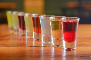 Küçük kadehlerle tentür alkoliği. Doğal meyve alkollü içecekler, bulanık arka planda ahşap bir masada servis edilen içkiler. Ahududu, çilek ve diğer meyveler, organik alkol özü..