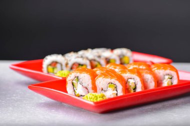 Siyah arka planda kırmızı tabakta servis edilen çeşitli suşi yemekleri. Geleneksel Japon mutfağı, California ya da Philadelphia suşi ruloları. Dikey pankart.