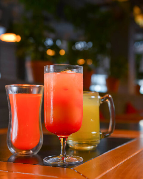 Three cocktails drinks on wooden table at bar indoors. Delicious fruit drinks for refreshment. Alcohol beverage in bar or restaurant. Vertical banner.
