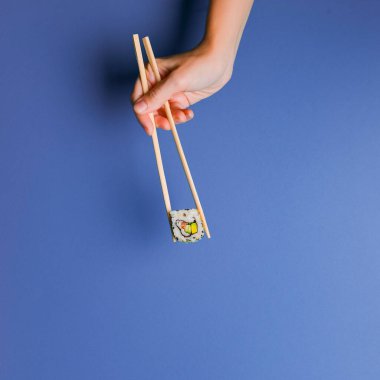 Canlı suşi seti, yaratıcı fikir. Sushi 'yi yemek çubuğunda, elinde tutarak. Geleneksel Japon mutfağı kavramı. Susam tohumları serpiştirilmiş. Parlak renkli arkaplanda. Boşluk afişini kopyala.