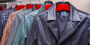 Mağazadaki askıda asılı siyah ve taçlı erkek giysileri. Erkekler için farklı renkte yay deri ceket koleksiyonu. Kapatın. Mevsimlik giysiler indirimde. Düşük fiyat, çeşitlilik.