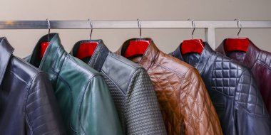 Mağazadaki askıda asılı siyah ve taçlı erkek giysileri. Erkekler için farklı renkte yay deri ceket koleksiyonu. Kapatın. Mevsimlik giysiler indirimde. Düşük fiyat, çeşitlilik.