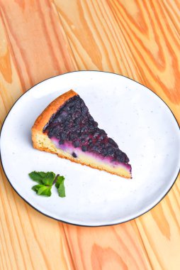 Kırsal ahşap arka planda beyaz bir tabakta yaban mersinli cheesecake dilimi. İtalyan mutfağı konsepti, mevsimlik sonbahar menüsü. Kapat..