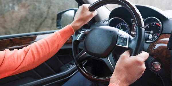 Adult man driving a car, close up on hands holding a steering wheel. Driving examination, exam, driving license. Man in a car travelling, travel concept.