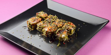 Suşi seti parlak pembe arka planda siyah kare bir tabakta servis edilir. Geleneksel Japon mutfağı, suşi dürümleri. Lezzetli yemek..