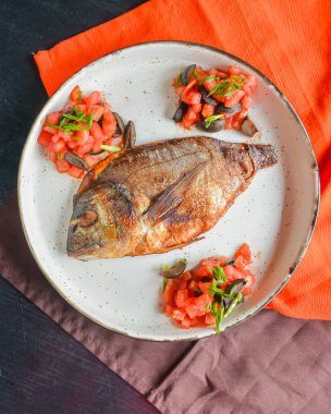 Taze otlu kızarmış balık, domates ve zeytin siyah rustik ahşap masa zemininde ve kırmızı ve kahverengi masa örtüsünde servis edilir. Akşam yemeği, geleneksel yemekler..