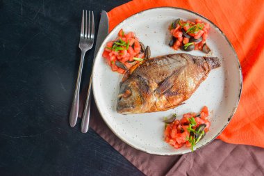 Taze otlu kızarmış balık, domates ve zeytin siyah rustik ahşap masa zemininde ve kırmızı ve kahverengi masa örtüsünde servis edilir. Akşam yemeği, geleneksel yemekler..