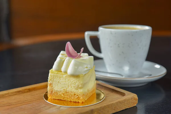 A cup of coffee and light vanilla dessert with cinnamon served on a rustic wooden board over black wooden table. Coffee time, sweet sugary snack.