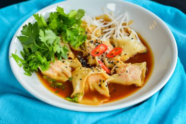 Taze maydanozlu haşlanmış et köftesi, soya sosu ve susam tohumları. Akşam yemeği için nefis yemekler, geleneksel yemekler. Beyaz bir kâsede, açık mavi masa örtüsüyle siyah, ahşap bir masanın üzerinde servis edilmiş..