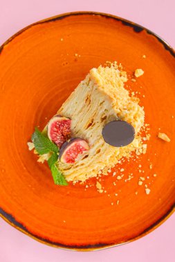 Bir parça taze incir meyveli Napolyon keki ve parlak turuncu bir tabakta servis edilen bir parça çikolata pastel pembe arka planda. Çay ya da kahve için lezzetli bir tatlı..