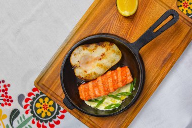 Ahşap bir tavada servis edilen yarım armutla ızgara somon bifteği. Ukrayna mutfağı konsepti, geleneksel masa örtüsü. Lezzetli yemek fikri..