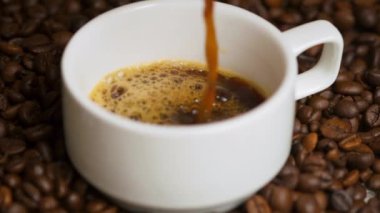 Kahveyi fincana dolduruyorum. Kahve çekirdeğinin üzerinde küçük beyaz bir fincanda Espresso kahvesi. Kahvaltı konsepti, sade kahve ve beyaz bardak. Seçici odak, kapat.