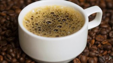 Kahve fincanda. Kahve çekirdeğinin üzerinde küçük beyaz bir fincanda Espresso kahvesi. Kahvaltı konsepti, sade kahve ve beyaz bardak. Seçici odak, kapat.