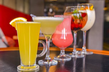 Kokteyller masada. Farklı renkte içecekler, farklı bardaklarda, koyu ahşap masada, bulanık restoran arka planında. Bar konsepti, alkol içecekleri.