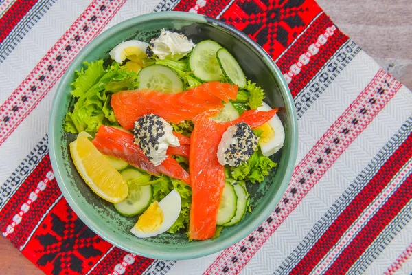 Close up of smoked salmon salad with boiled eggs, cucumbers, cream cheese with sesame seeds and a piece of lemon. Delicious fish salad for dinner.