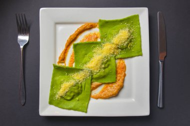 İçinde ıspanak ve et olan yeşil ravioli ve üstünde siyah zemin üzerinde beyaz kare tabakta servis edilen parmesan peyniri. Lezzetli İtalyan mutfağı konsepti.