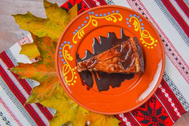 Geleneksel Ukrayna masa örtüsünün üzerinde parlak turuncu bir tabakta servis edilen çikolata soslu vanilyalı karamel ve çikolatalı cheesecake. Çay ya da kahve için lezzetli bir tatlı..