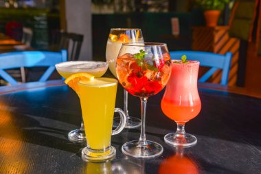 Kokteyller masada. Farklı renkte içecekler, farklı bardaklarda, koyu ahşap masada, bulanık restoran arka planında. Bar konsepti, alkol içecekleri.