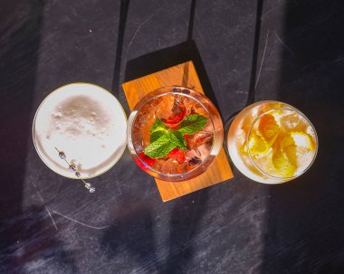 Kokteyller masada. Farklı renkte içecekler, farklı bardaklarda, koyu ahşap masada, bulanık restoran arka planında. Bar konsepti, alkol içecekleri.