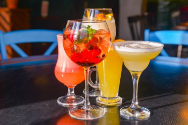 Kokteyller masada. Farklı renkte içecekler, farklı bardaklarda, koyu ahşap masada, bulanık restoran arka planında. Bar konsepti, alkol içecekleri.