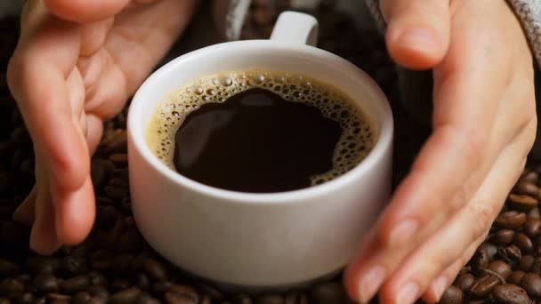 咖啡豆背景上有一杯黑咖啡的手的侧面视图 一杯白咖啡 优雅的女人手拿着小杯咖啡 有选择的重点 — 图库视频影像