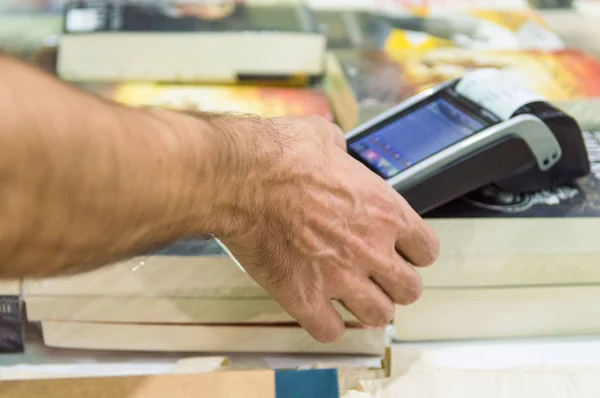 Close up of male hand using credit card swiping machine to pay. Man entering credit card code in POS machine in a book store.