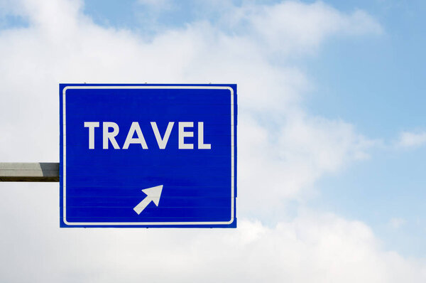 Blue road sign displaying Travel word on blue sky and white clouds background